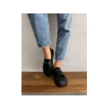 Mocasín Glow negro de Beflamboyant con flecos y hebilla dorada, puesto con vaqueros sobre un banco de madera