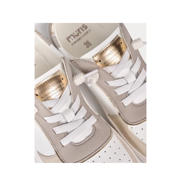 Detalle de zapatillas Muris blancas con piezas taupe, lengüeta dorada y cordones elásticos blancos con tope